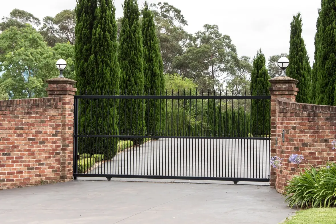 Black iron driveway gate between stone columns.