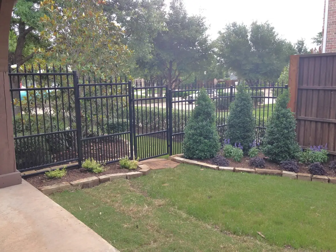 Black iron fence and gate beside a landscaped yard.