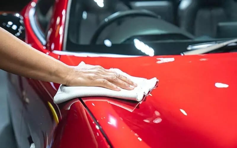 Hand wiping red sports car bonnet with microfibre cloth to showroom gloss