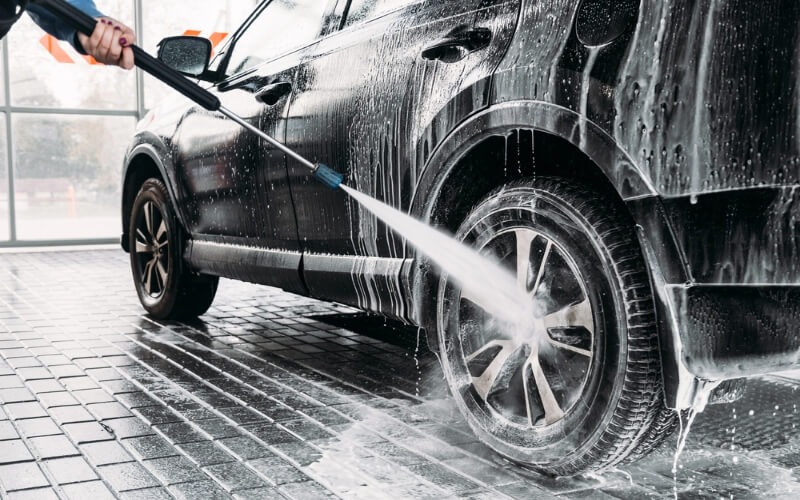 High-pressure foam wash and wheel arch cleaning on black car