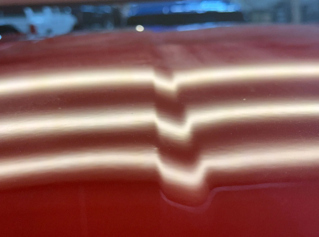 Same red vehicle panel under PDR reflection lighting after paintless dent repair