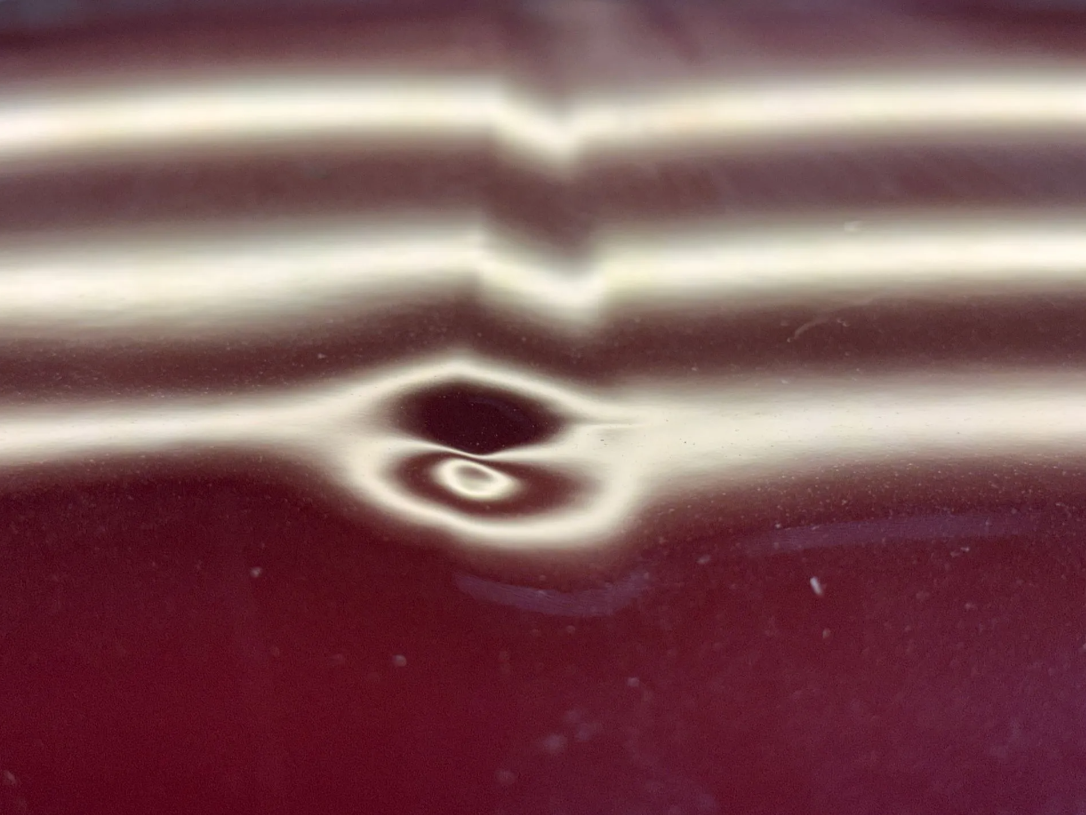 Close-up of a visible dent in a red vehicle panel before paintless dent repair