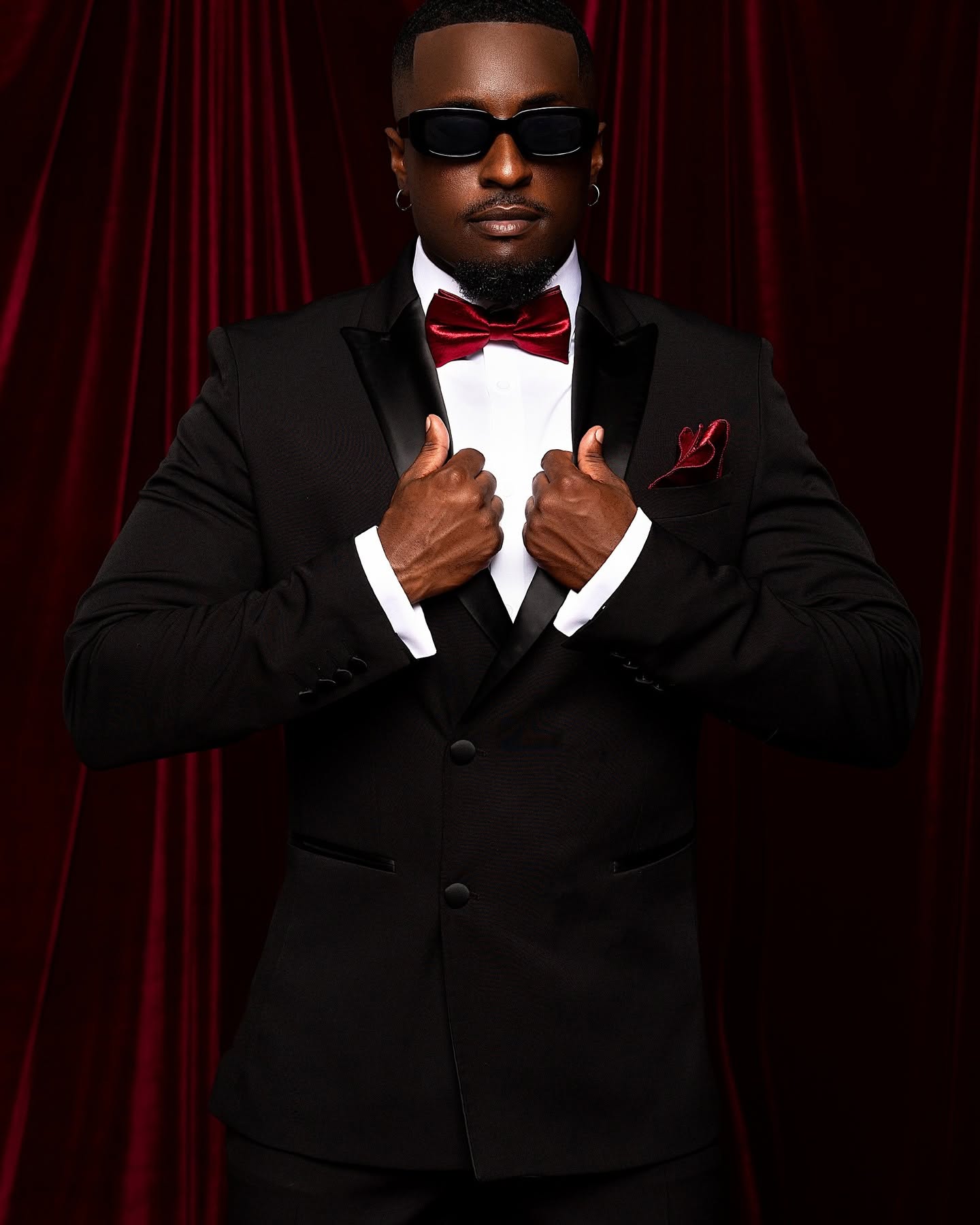 Luxury portrait of a man in a black tuxedo and burgundy bowtie against rich crimson curtains