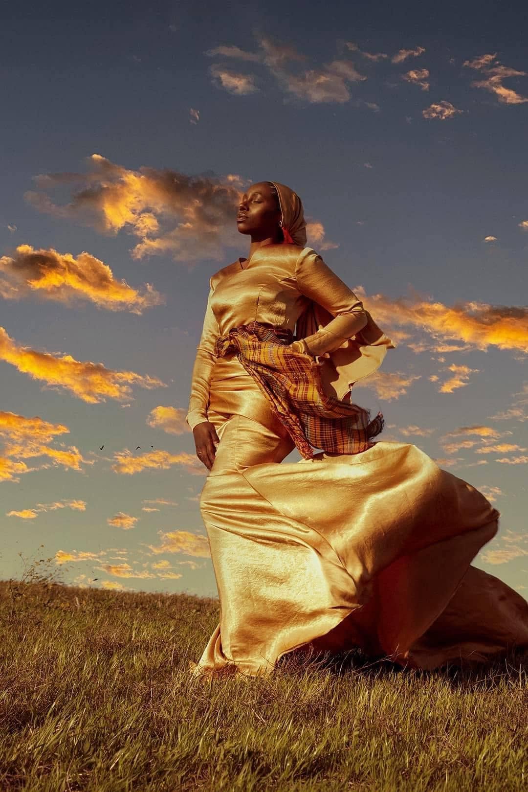 Editorial portrait in an open grassy field bathed in warm golden sunset light with satin dress