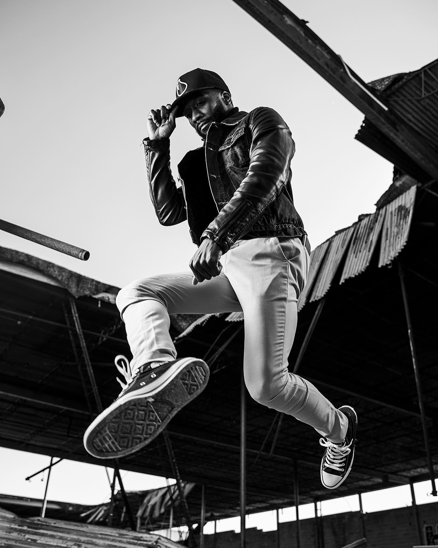 Black and white action portrait of a man suspended mid-air in front of an industrial structure
