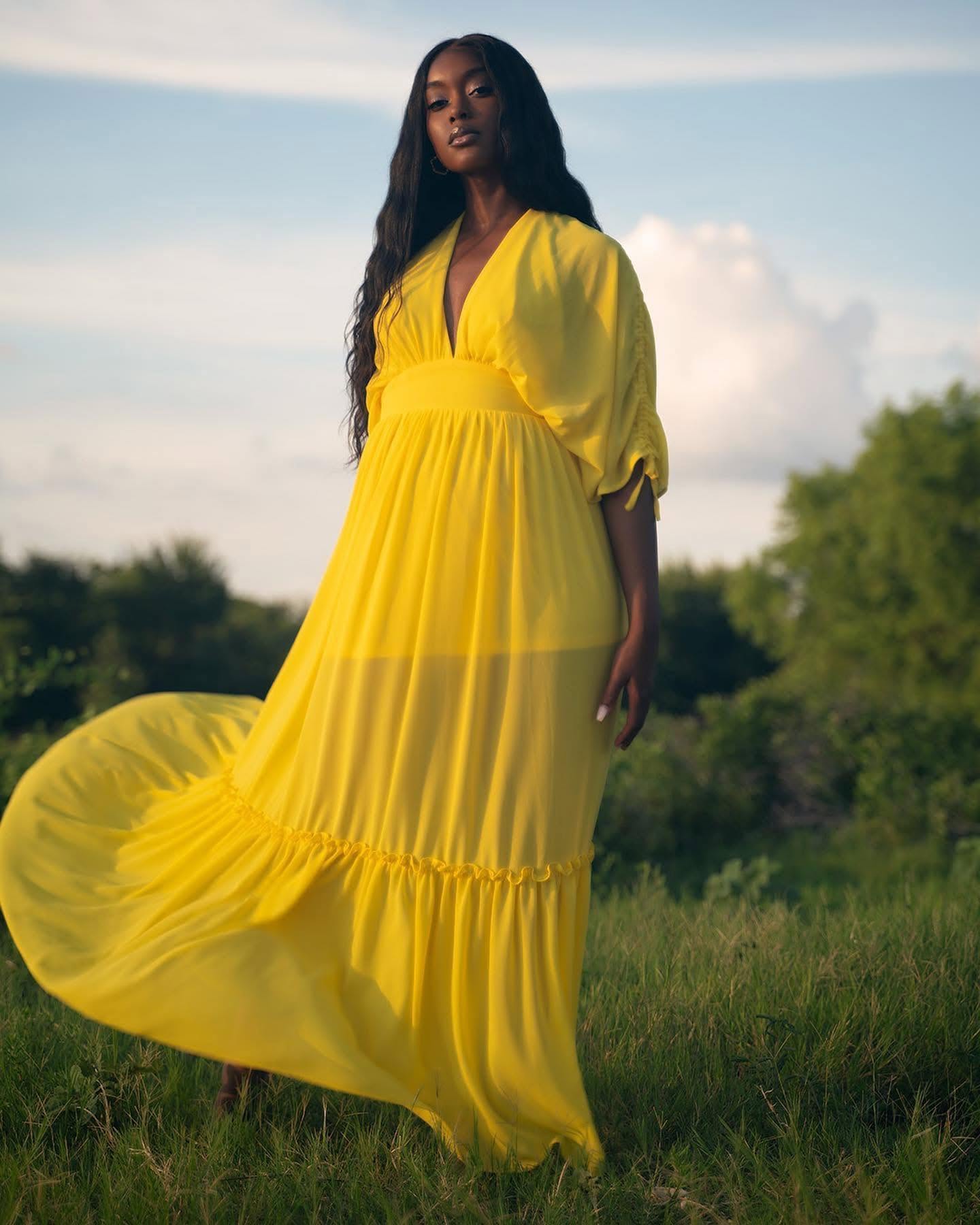 Outdoor portrait of woman in flowing vibrant yellow dress in sunlit open field