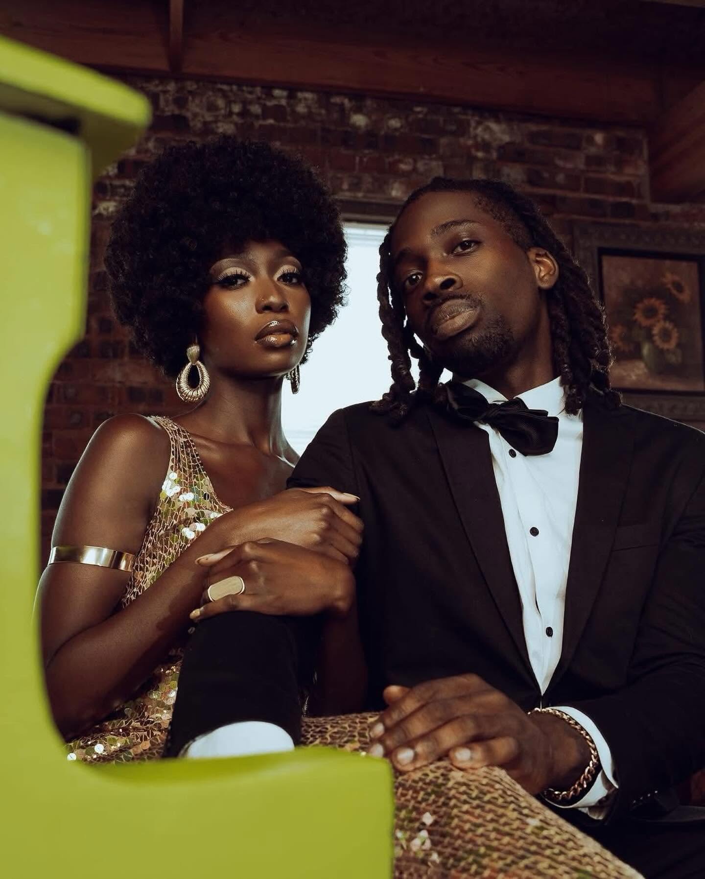 Editorial couple portrait in gold sequin gown and classic black tuxedo against exposed brick