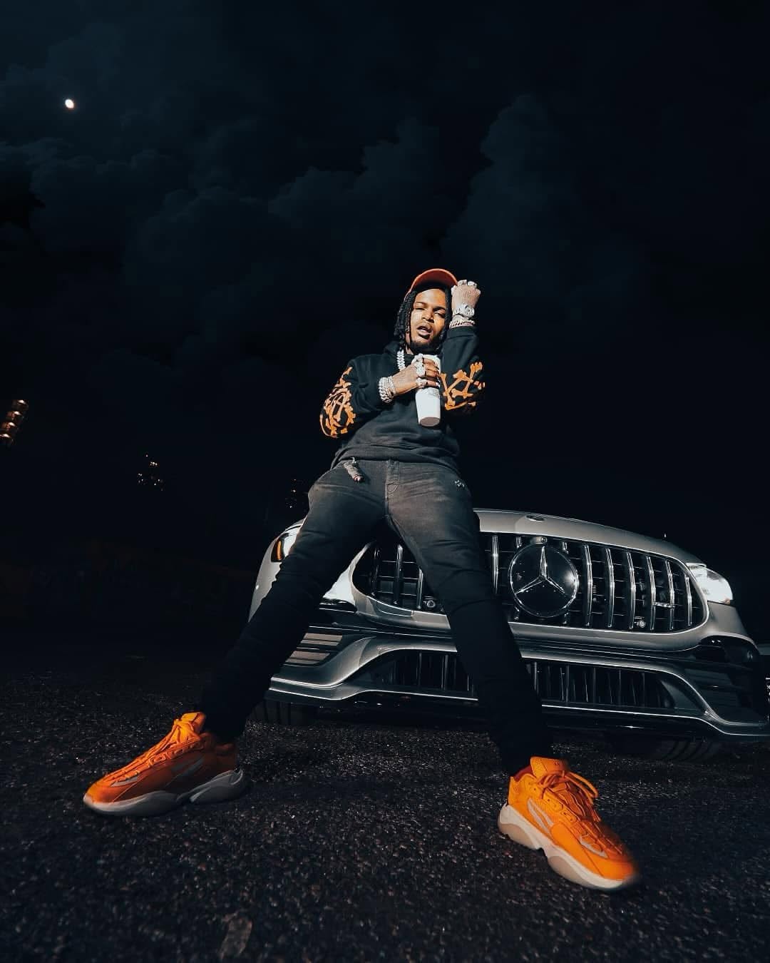 Editorial nighttime lifestyle portrait of man in black hoodie and orange sneakers leaning on a Mercedes AMG