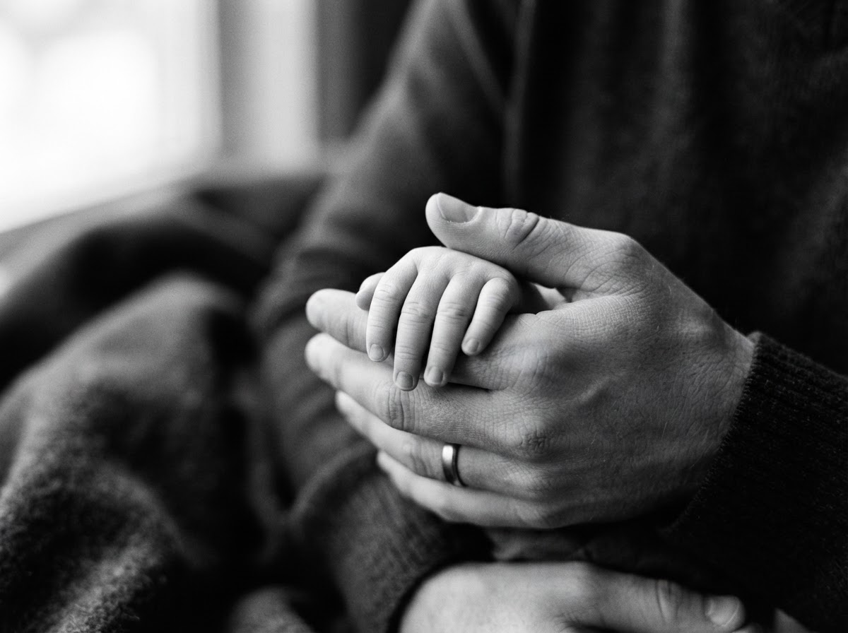 En nyfödd bebis lilla hand hållen i en vuxen hand — svartvitt