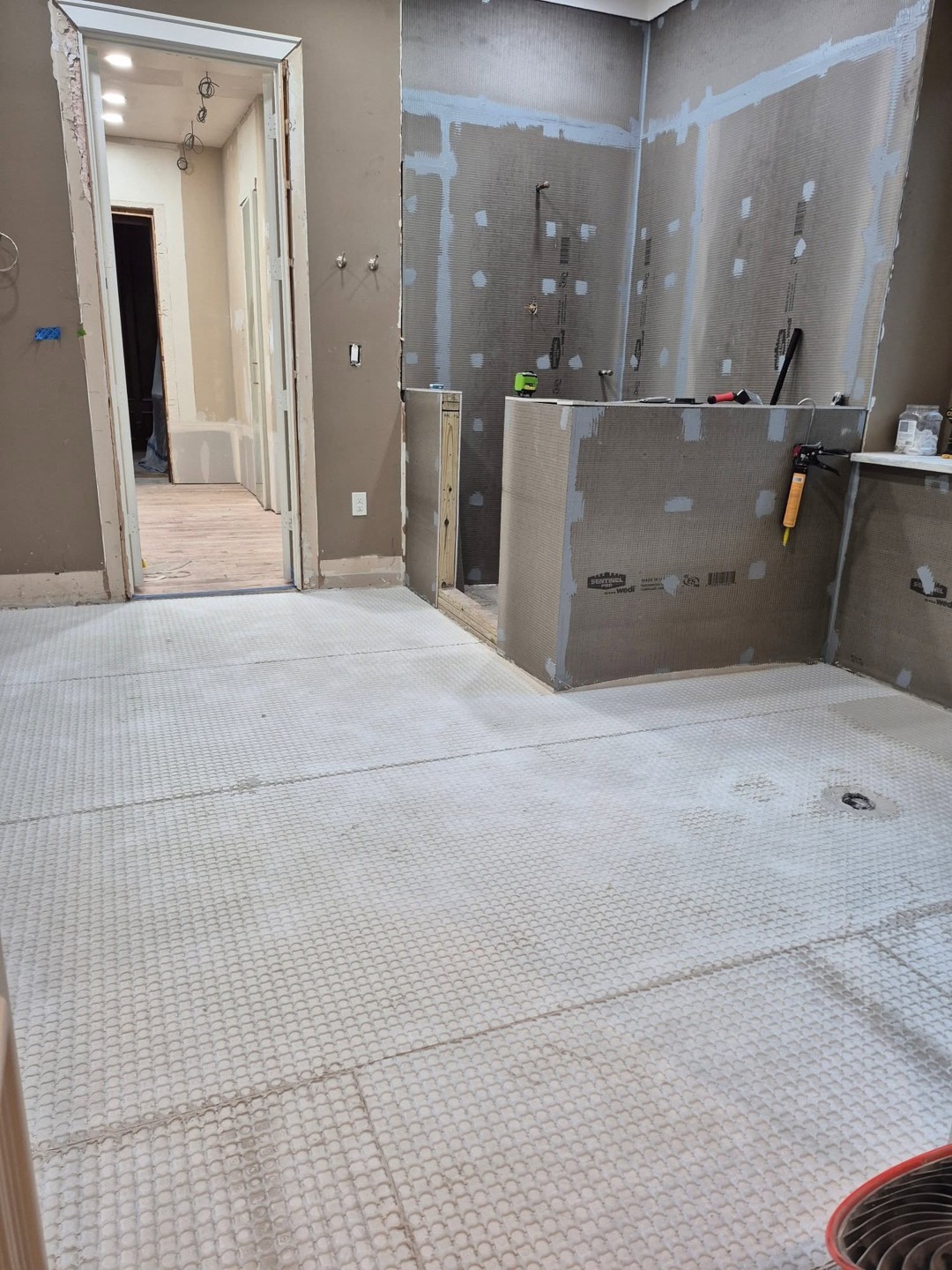 Steam shower interior with a built-in tile niche, stone bench, and floor-to-ceiling waterproofed tile