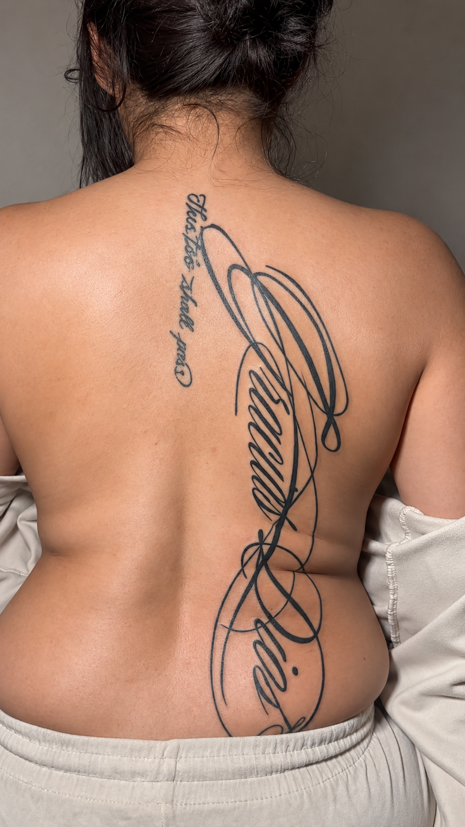 Large ornamental script tattoo running down the back