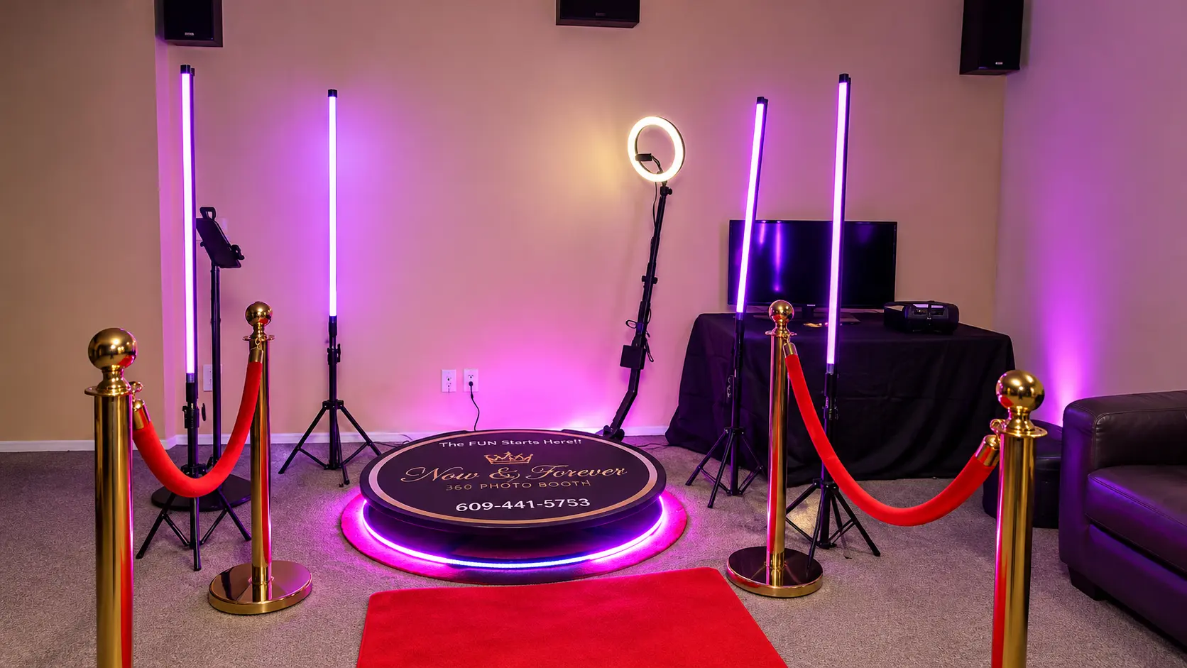 Now & Forever 360 photo booth setup with glowing neon tube lighting, VIP red velvet ropes, gold stanchions, ring light, and branded 360 platform
