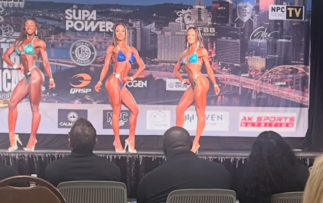 Three bikini competitors on stage under bright show lighting