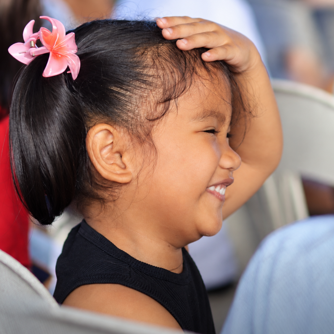 A young girl smiling brightly with a pink flower hair clip during a visit.