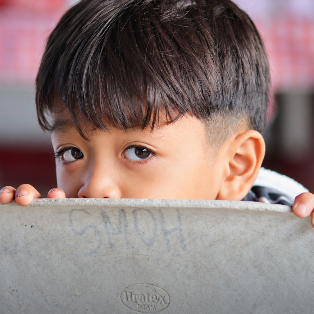 A young boy playfully peeking over a wall during a community gathering.