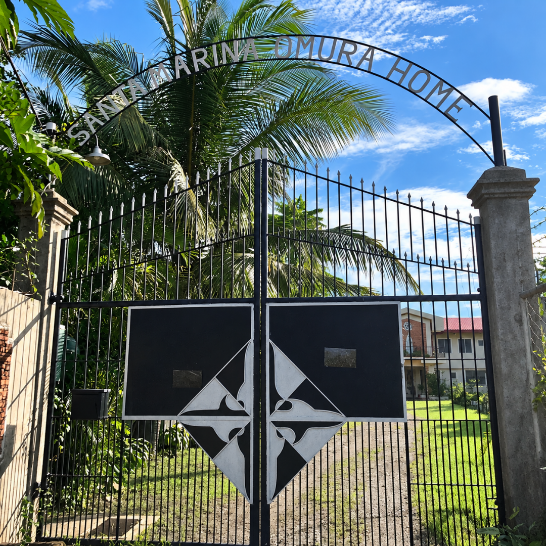 The entrance archway and wrought iron gate of Santa Marina Omura Home under a clear blue sky.