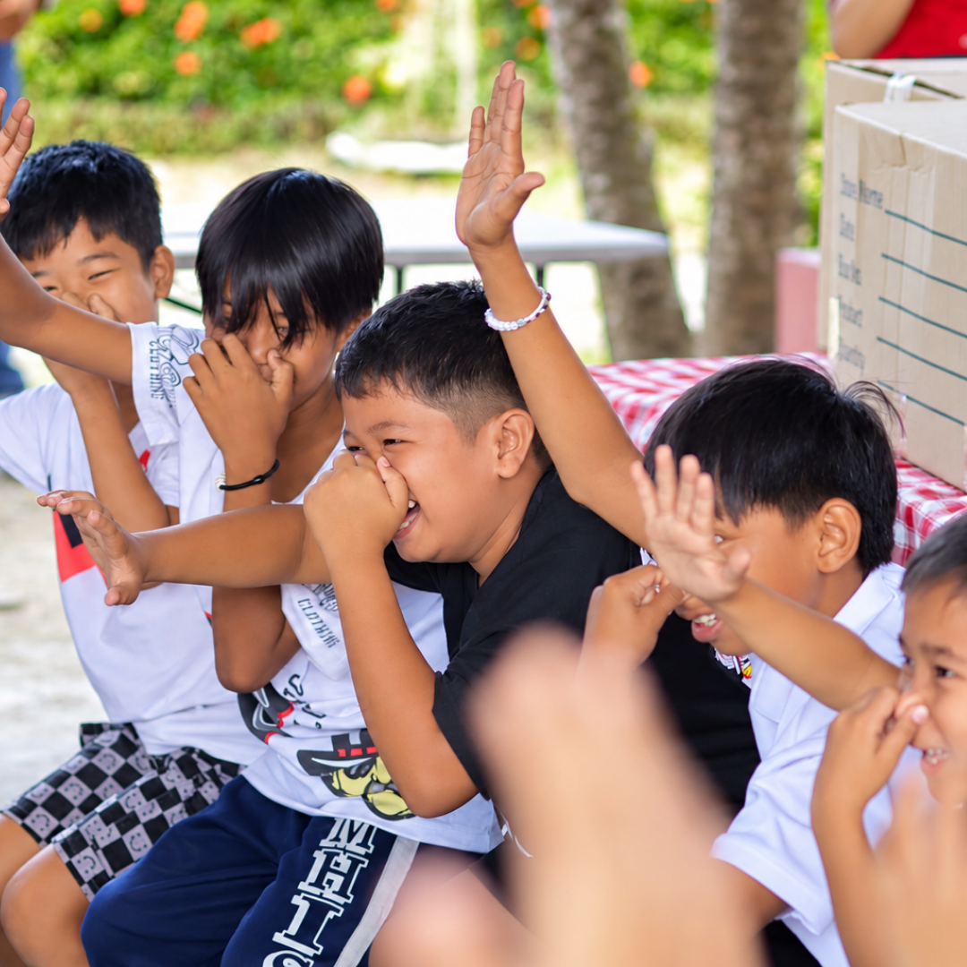 Children raising their hands and laughing during a fellowship activity at Omura Homes.