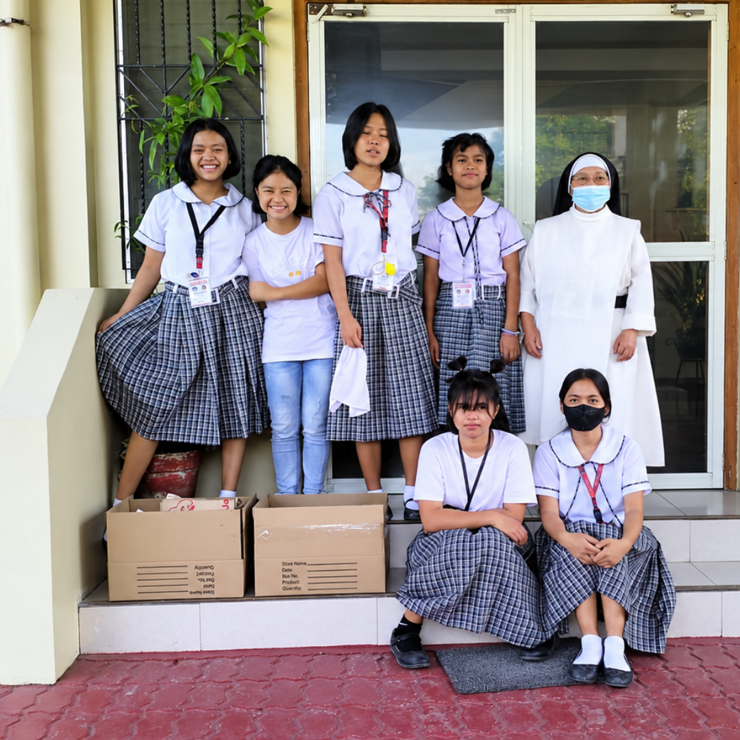 Students in school uniforms with care boxes and sister at the entrance of Omura Home.