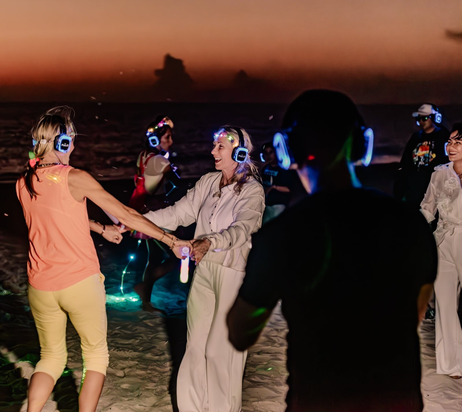 Runners dancing in glowing THE FIELD headsets on the beach at sunset