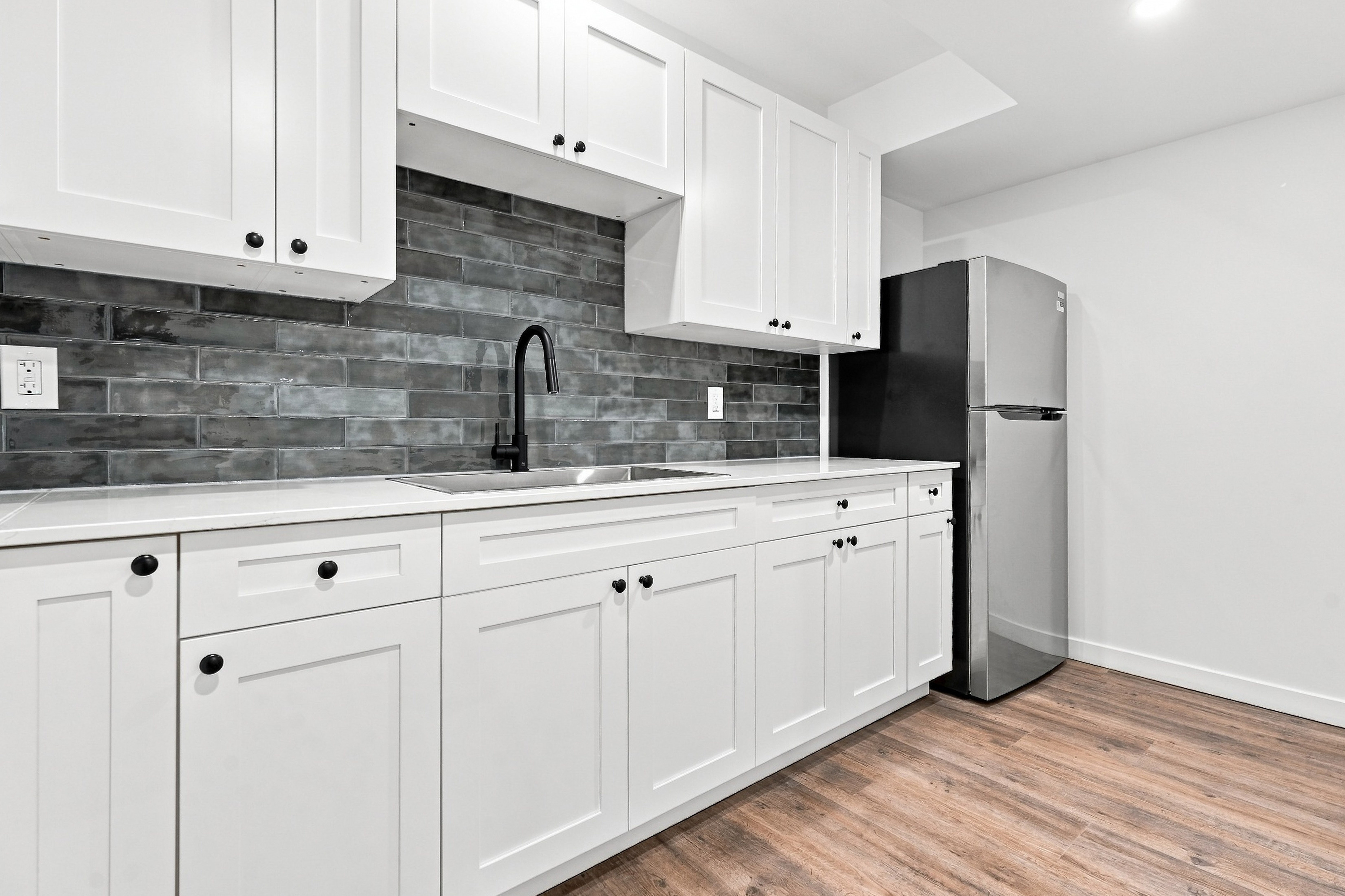 Kitchen sink, matte black faucet, tile backsplash, and stainless refrigerator