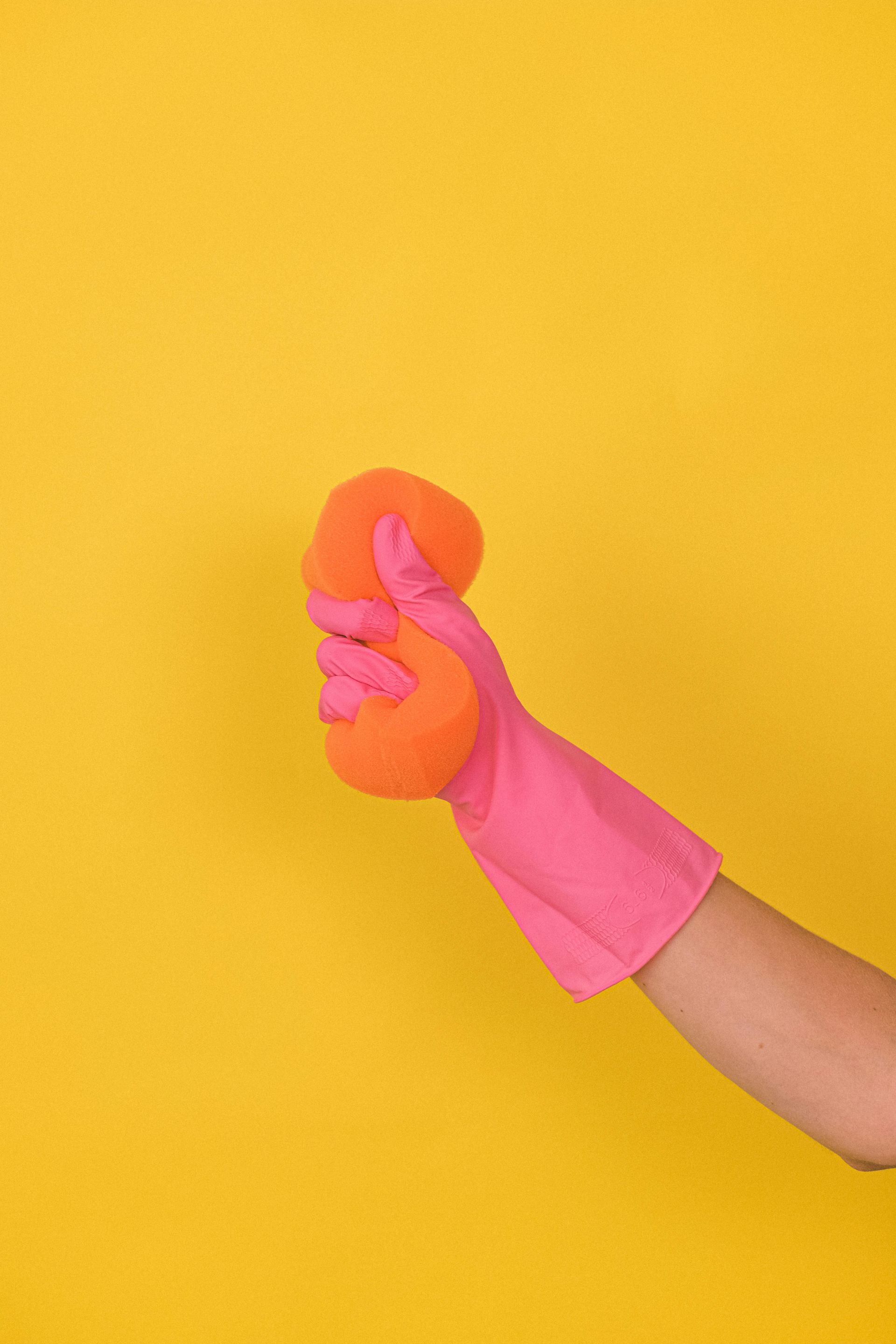 Pink glove holding an orange sponge on yellow background