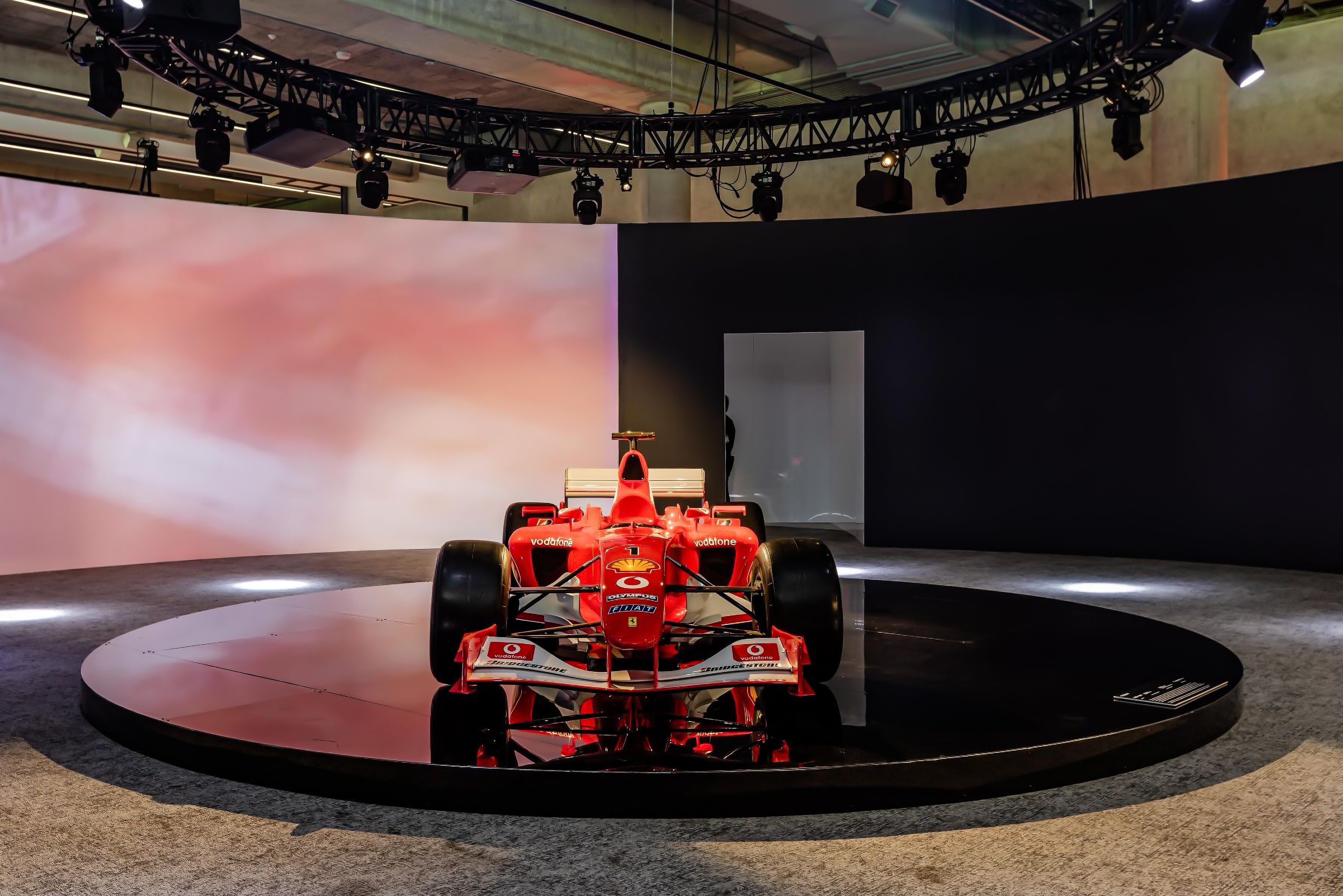 Ferrari Formula 1 showcase car on circular stage with curved backdrop and circular lighting truss