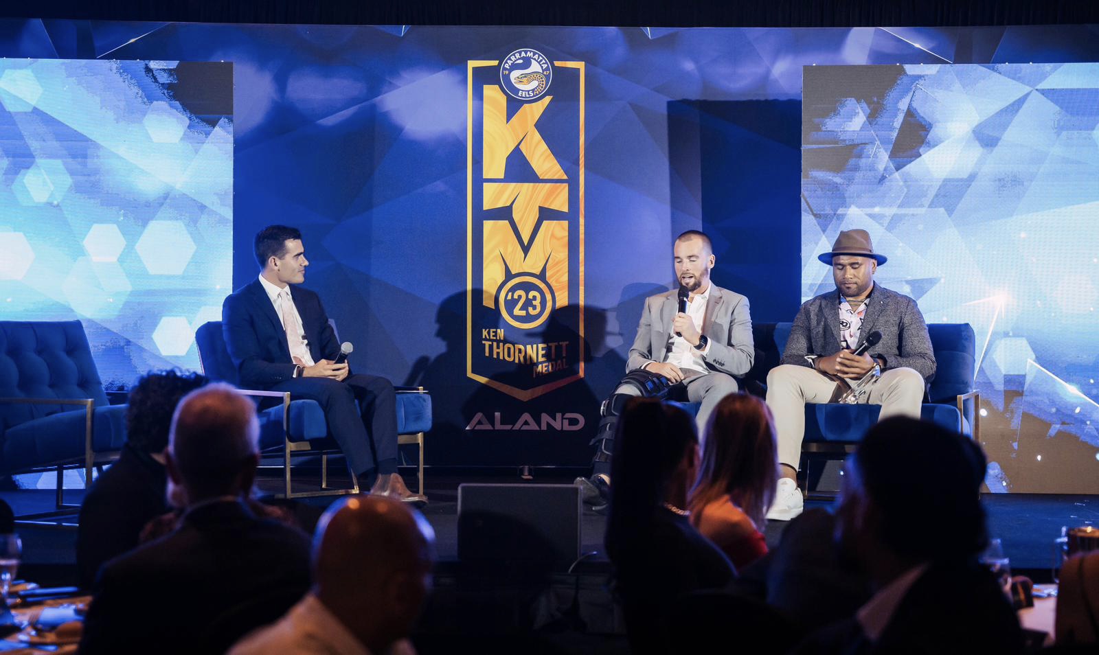 Ken Thornett Medal awards panel interview on stage with custom KTM backdrop, LED screens and blue stage lighting