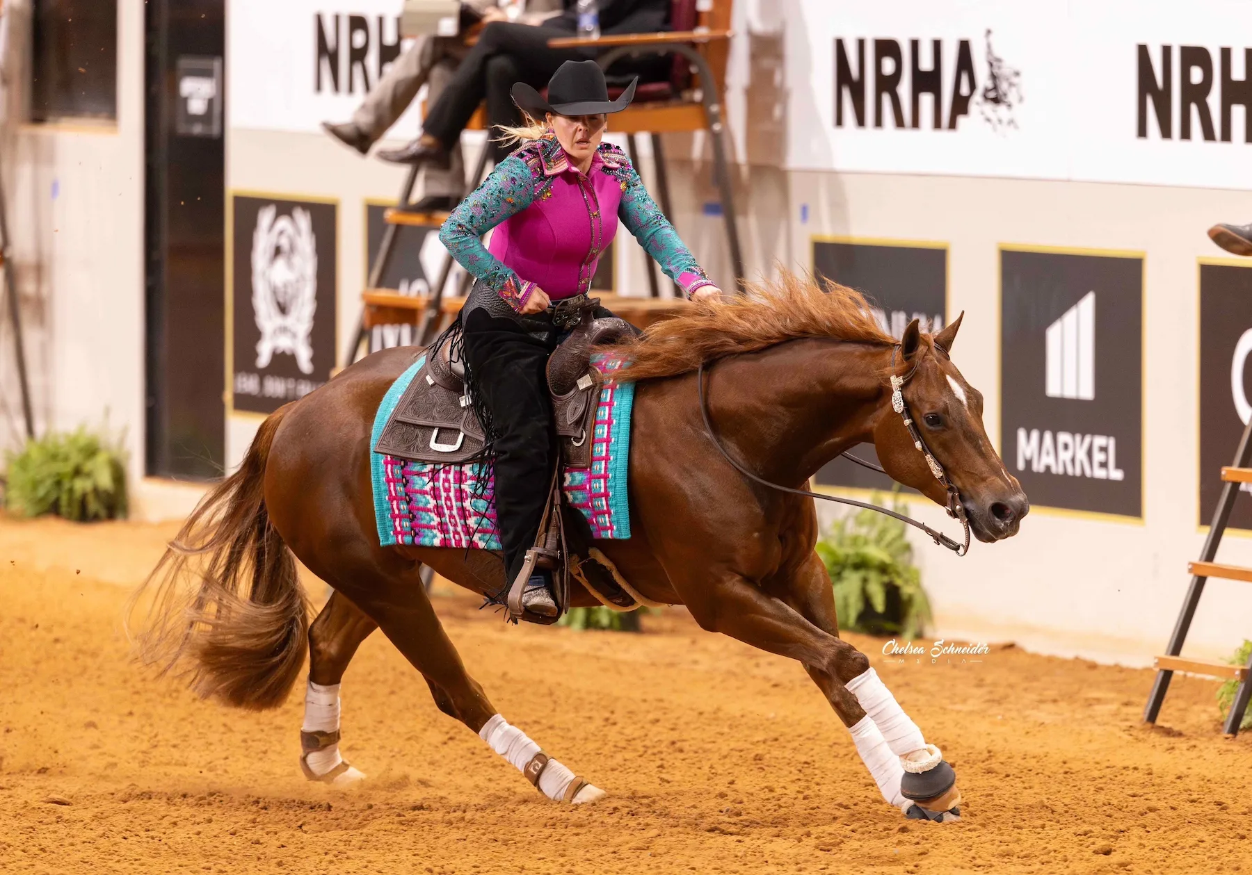 Allison Yeager riding a chestnut reining horse at an NRHA competition in magenta and teal show shirt
