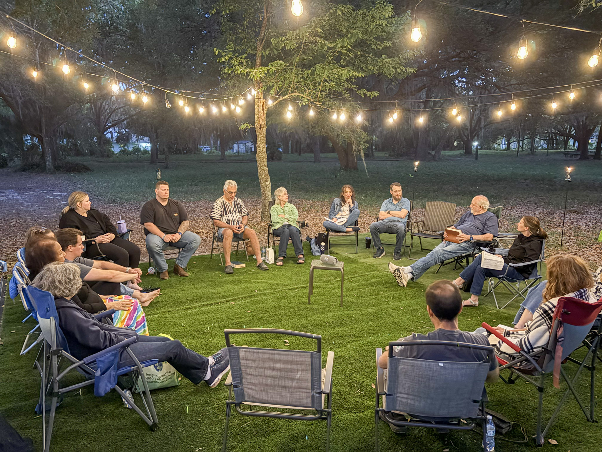 A circle of wooden and canvas chairs under a wide shade tree in soft evening light