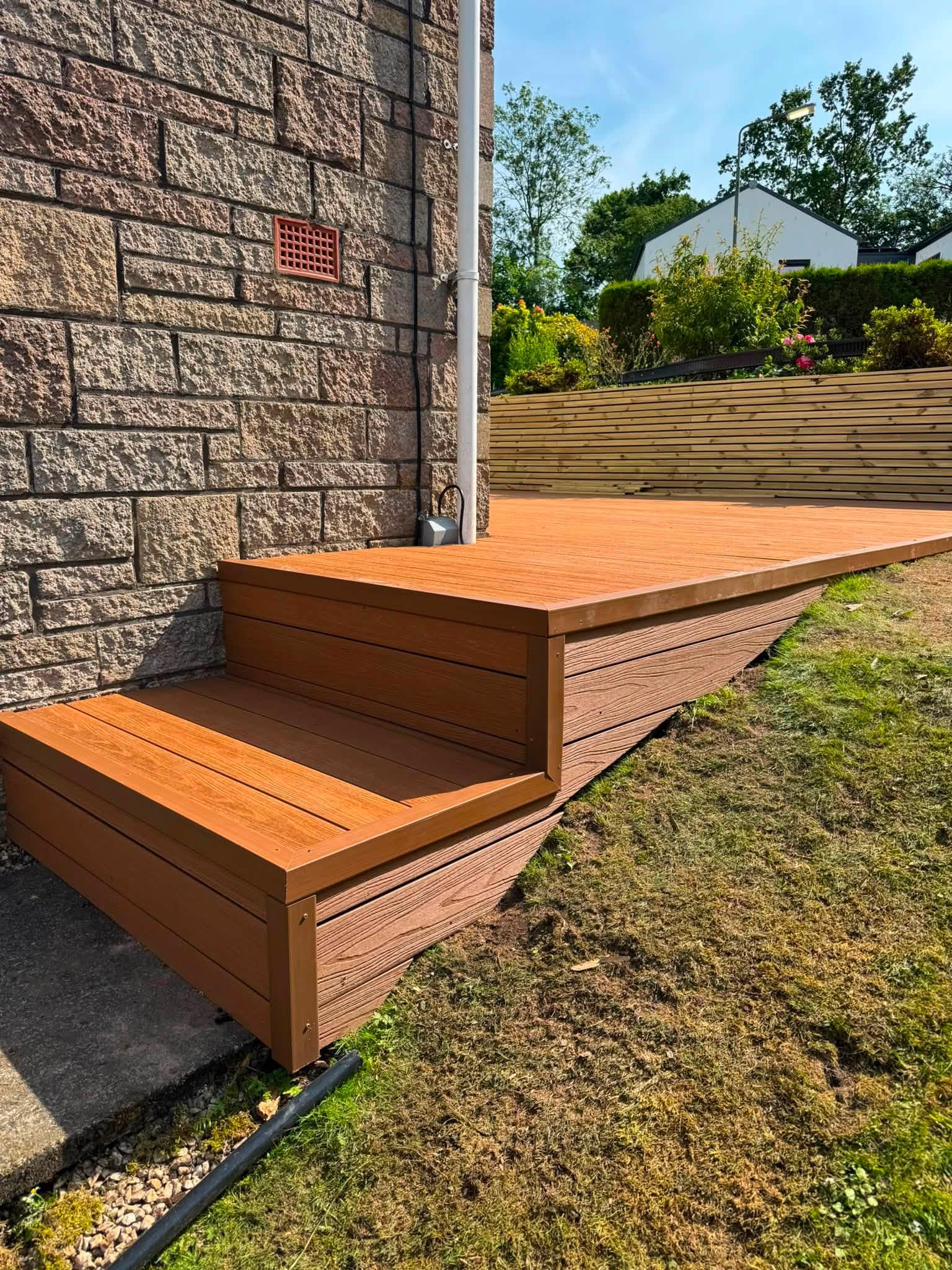 Custom composite garden decking with stepped entryway built against stone wall by SJ Joinery & Building