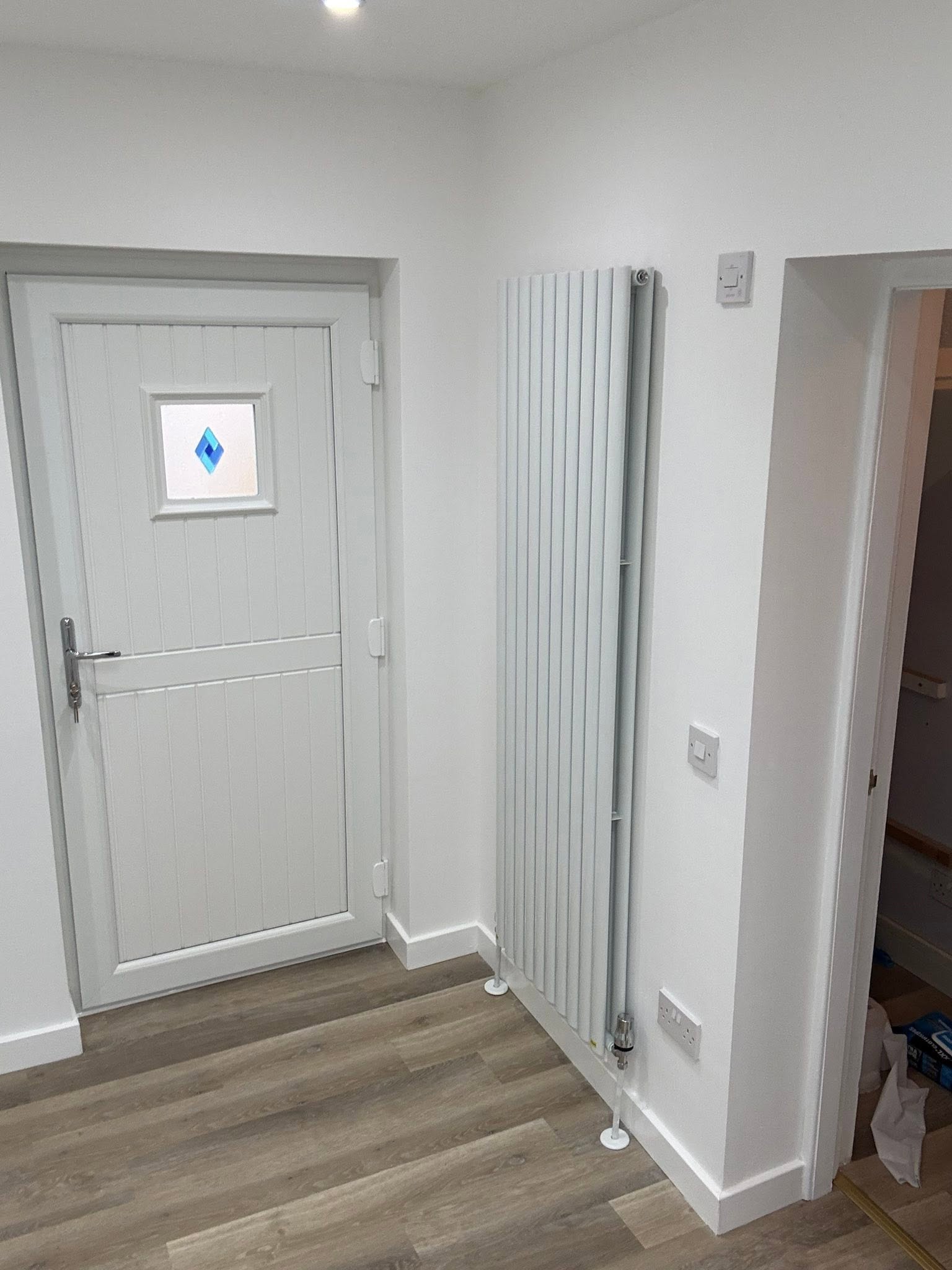 Modern entrance hallway with secure composite door, decorative diamond glass, tall vertical designer radiator and oak flooring by SJ Joinery & Building