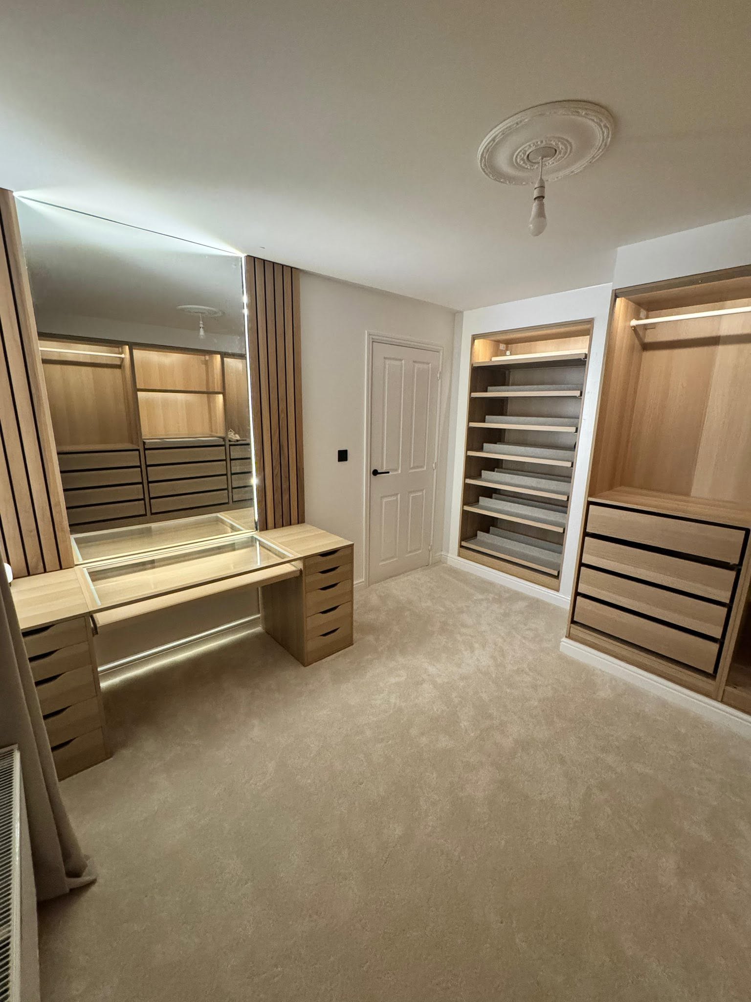 Custom fitted walk-in wardrobe and dressing room with oak shelving, fluted timber accents and integrated vanity lighting by SJ Joinery & Building