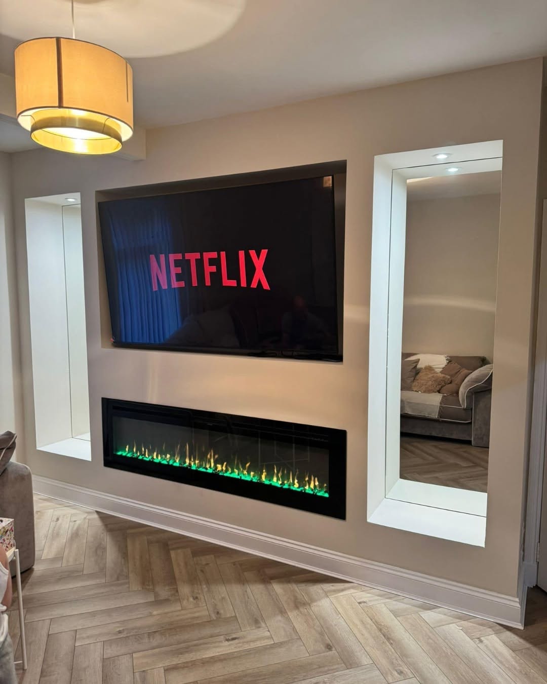 Modern recessed media wall with contemporary electric fire, illuminated twin vertical alcoves, and herringbone flooring by SJ Joinery & Building