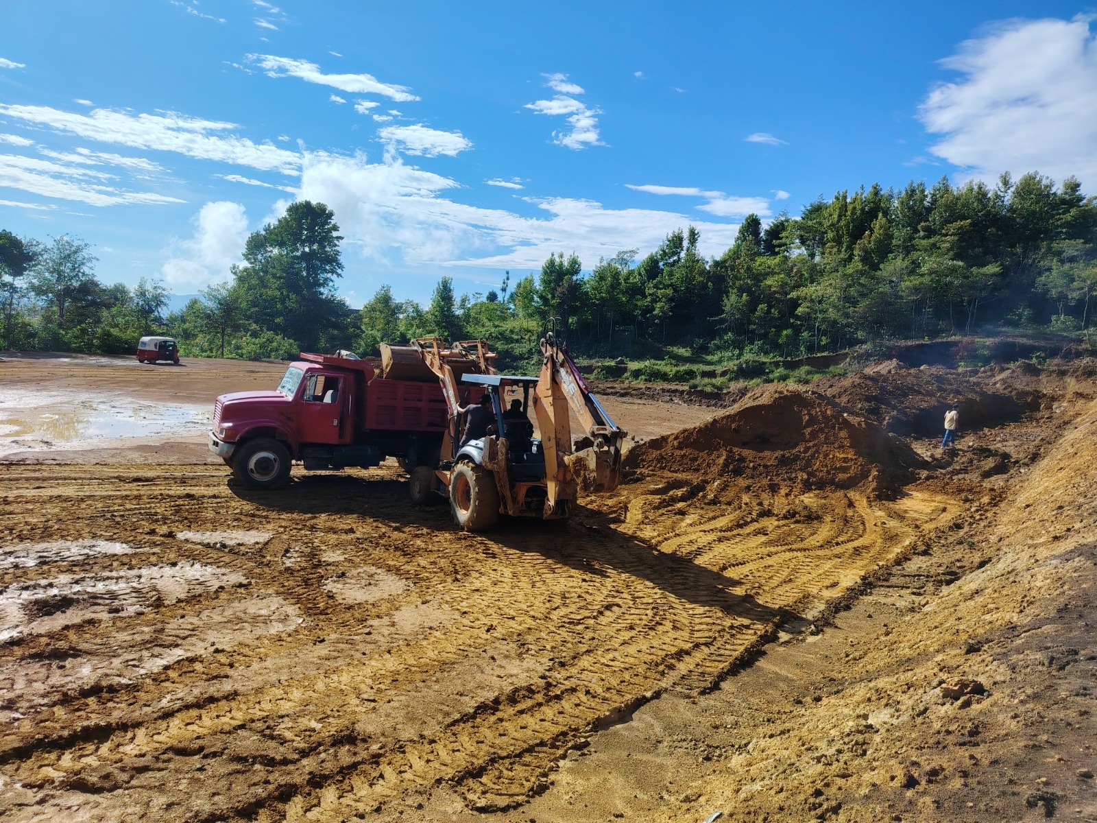 Retroexcavadora cargando material térreo en camión de volteo en obra vial