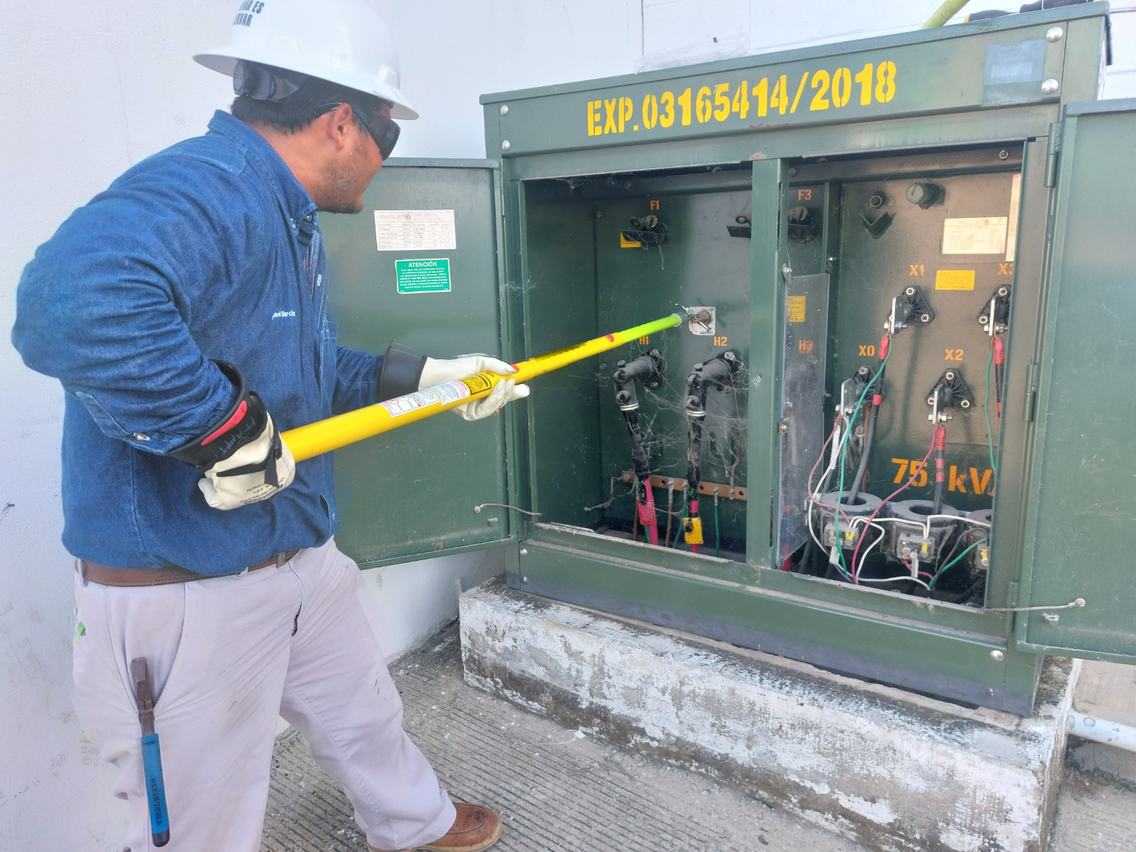 Técnico especialista con equipo de protección y pértiga realizando maniobra en transformador tipo pedestal de media tensión