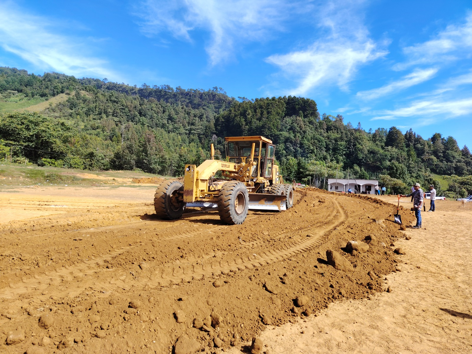 Motoniveladora Caterpillar conformando terracerías y trazo de camino vial con personal técnico