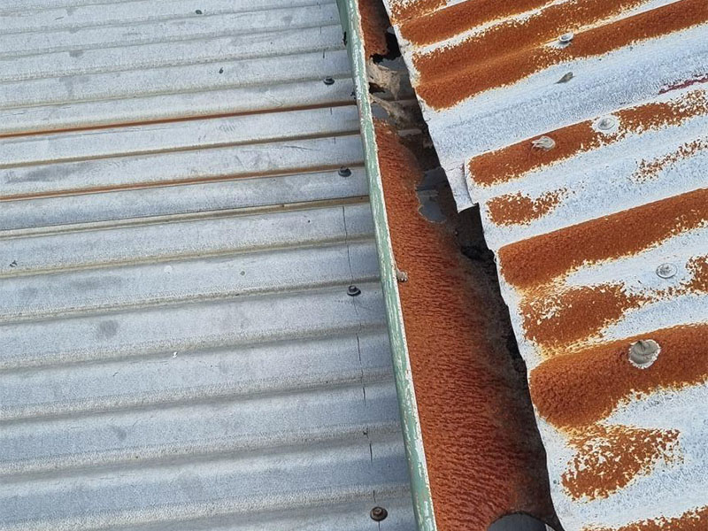 Severe rust, loose screws and patched flashing along a corrugated metal roof edge