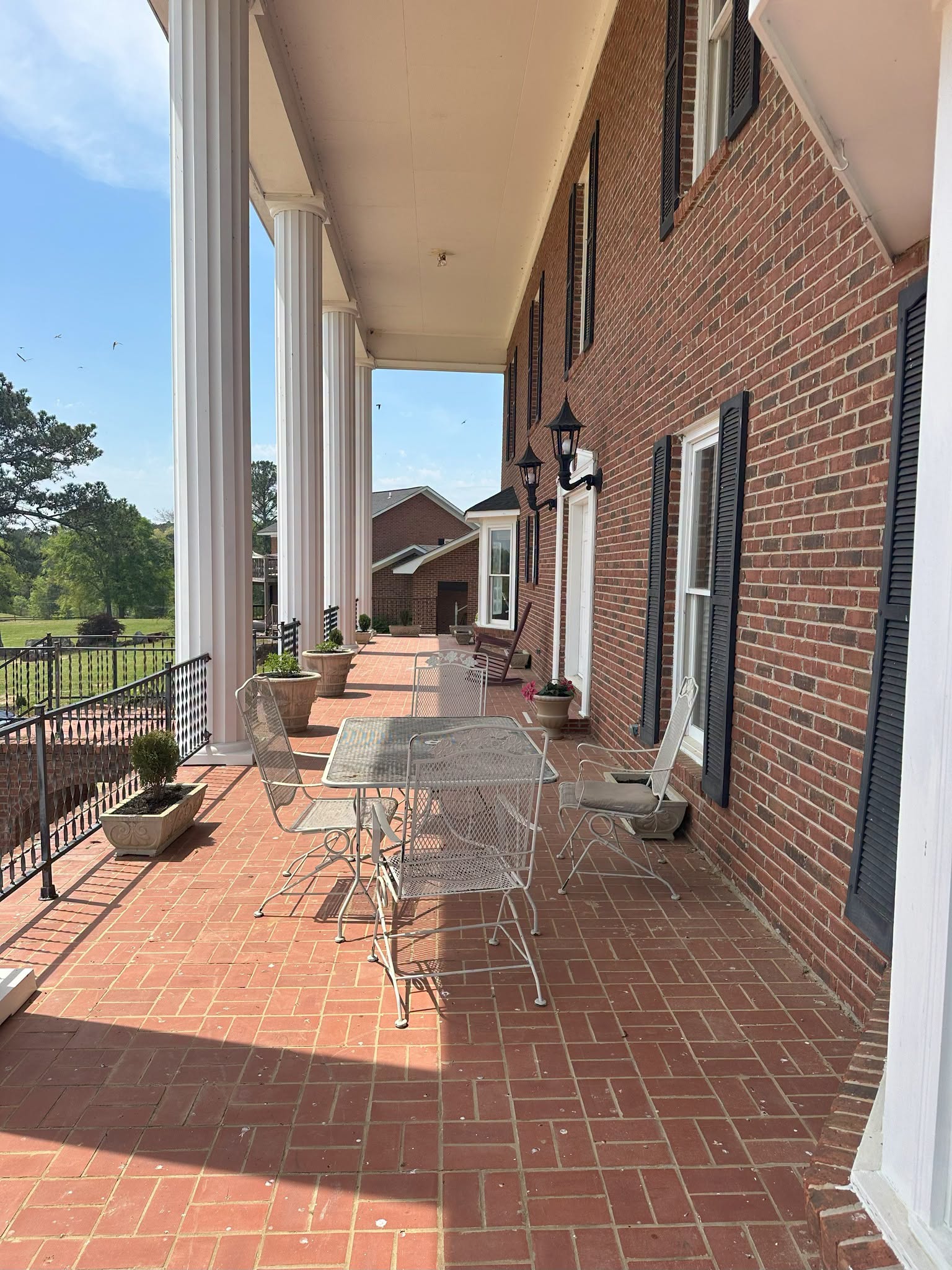 The Big House expansive brick porch with white columns, outdoor seating, and scenic grounds view