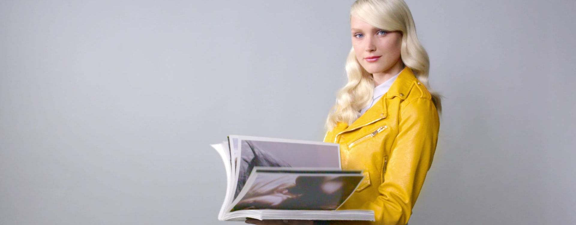 Model in yellow leather jacket reading branded magazine
