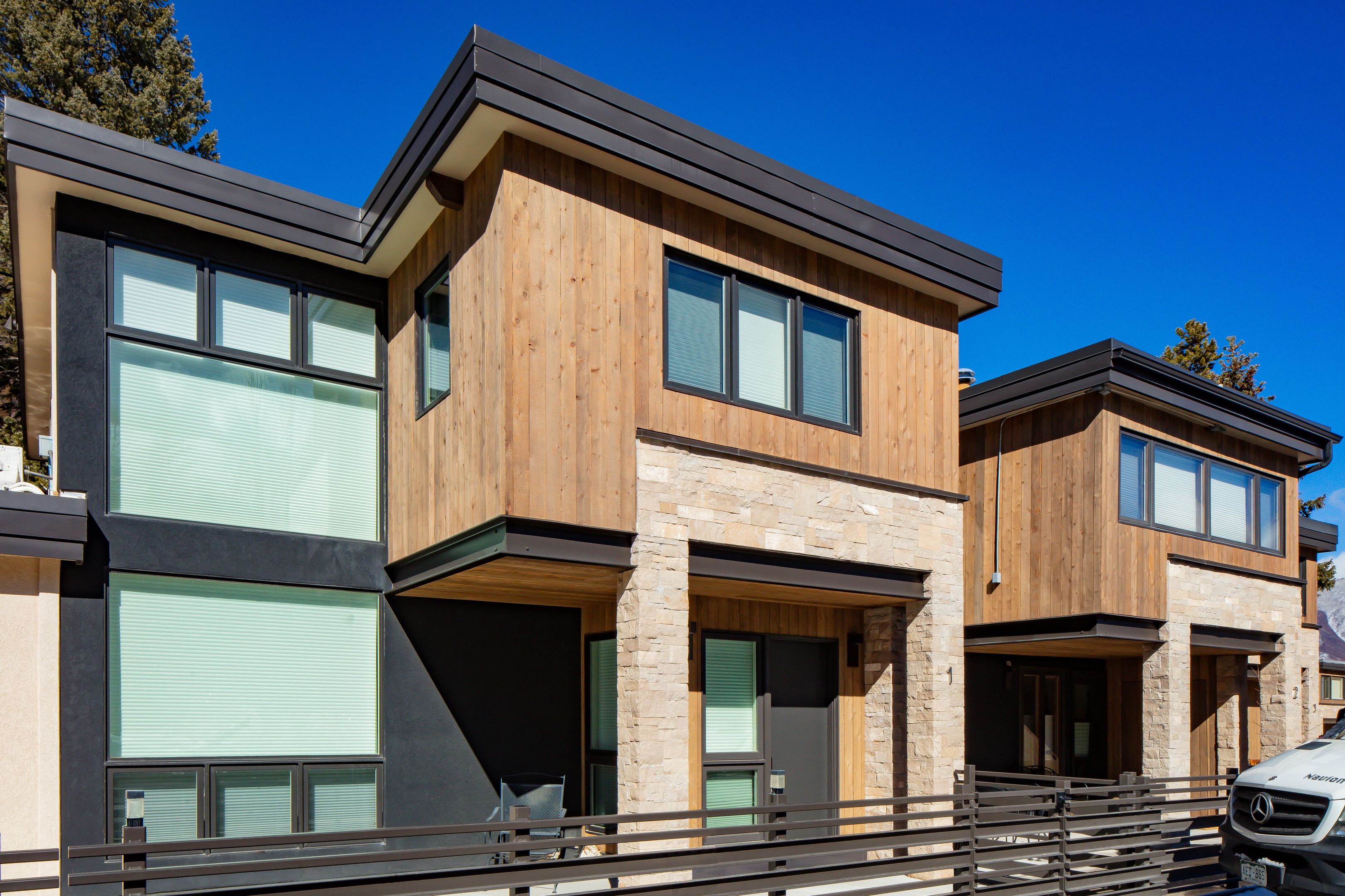 Wide townhome exterior elevation with horizontal metal perimeter fencing and alpine ridgeline — Highlands Villas, Aspen, CO