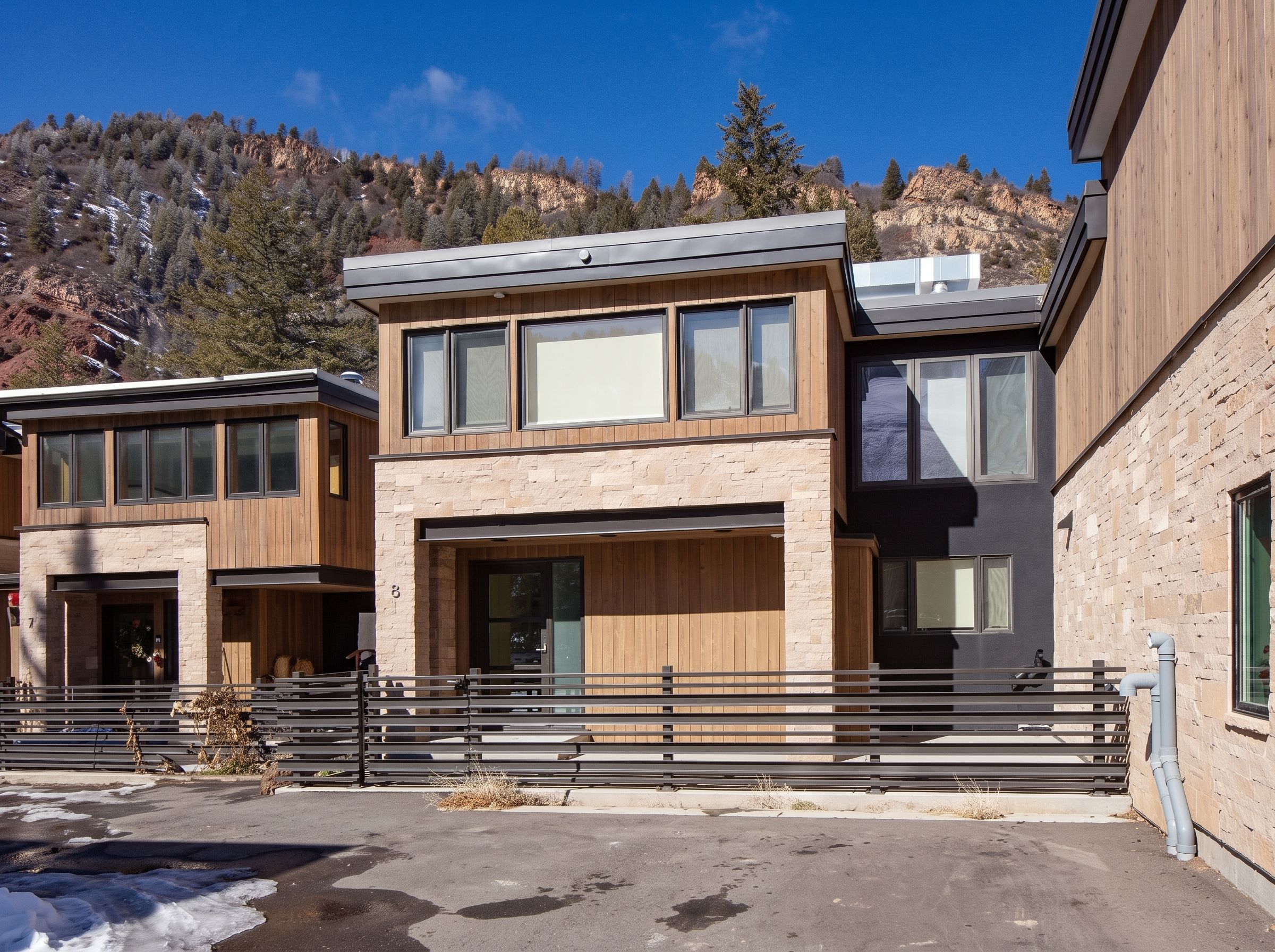 Unit 8 exterior elevation showcasing stone masonry, vertical timber siding, horizontal privacy fencing, and mountain backdrop — Highlands Villas, Aspen, CO