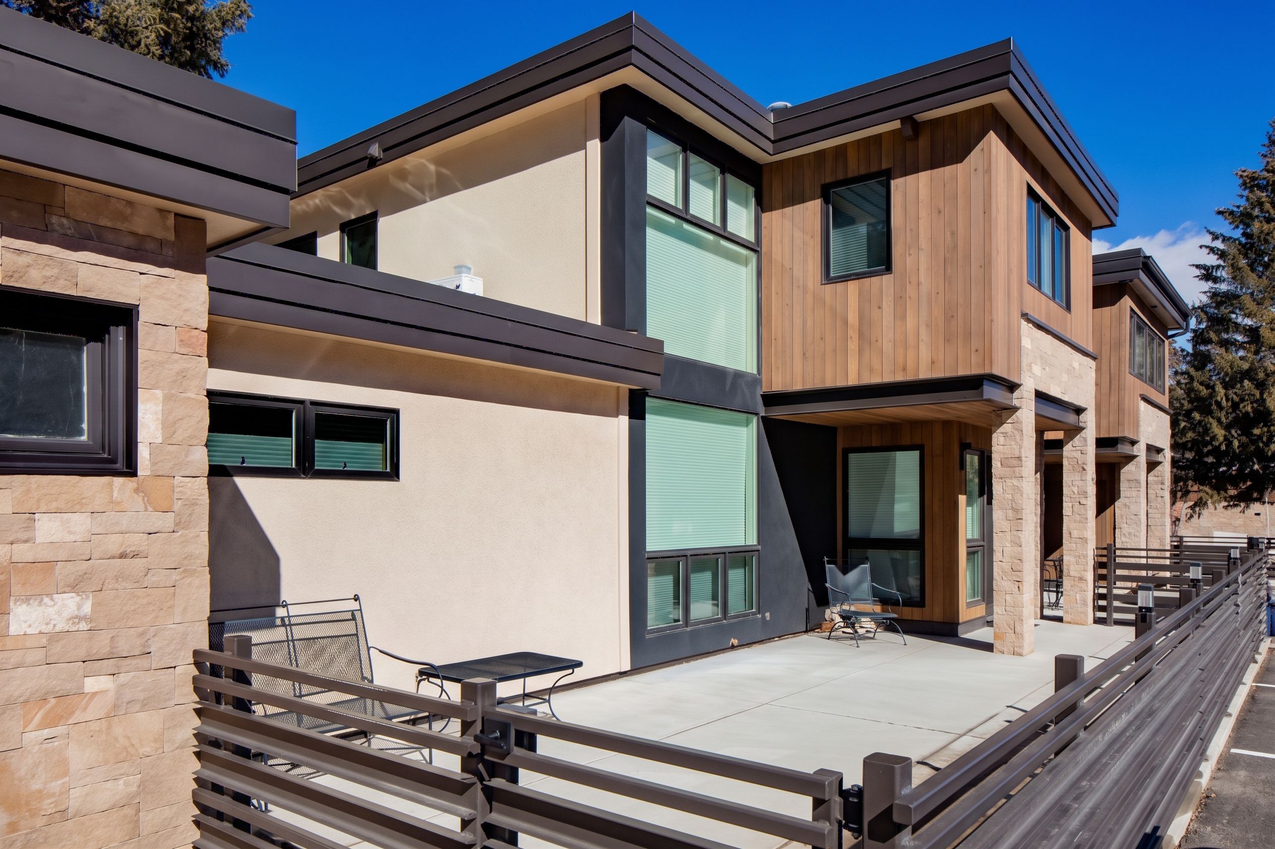 Angled patio and architectural view highlighting stucco, vertical timber siding, stone pillars, and enclosed concrete courtyard — Highlands Villas, Aspen, CO