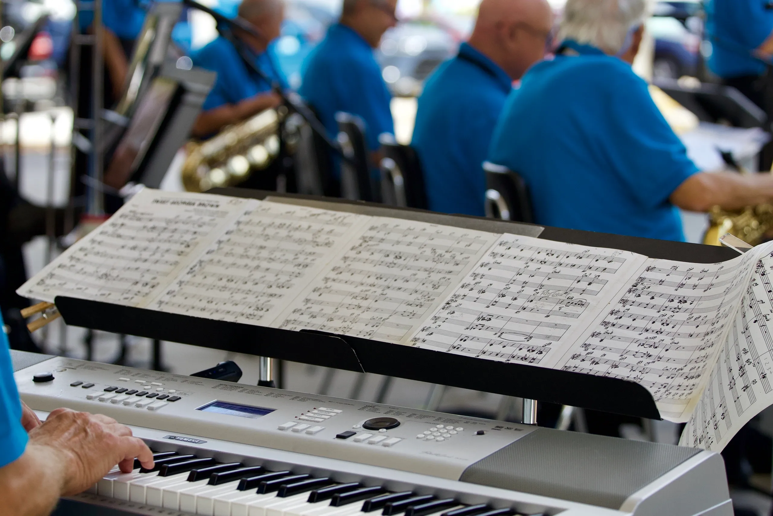 Pianist playing keyboard with sheet music and saxophone section during outdoor concert