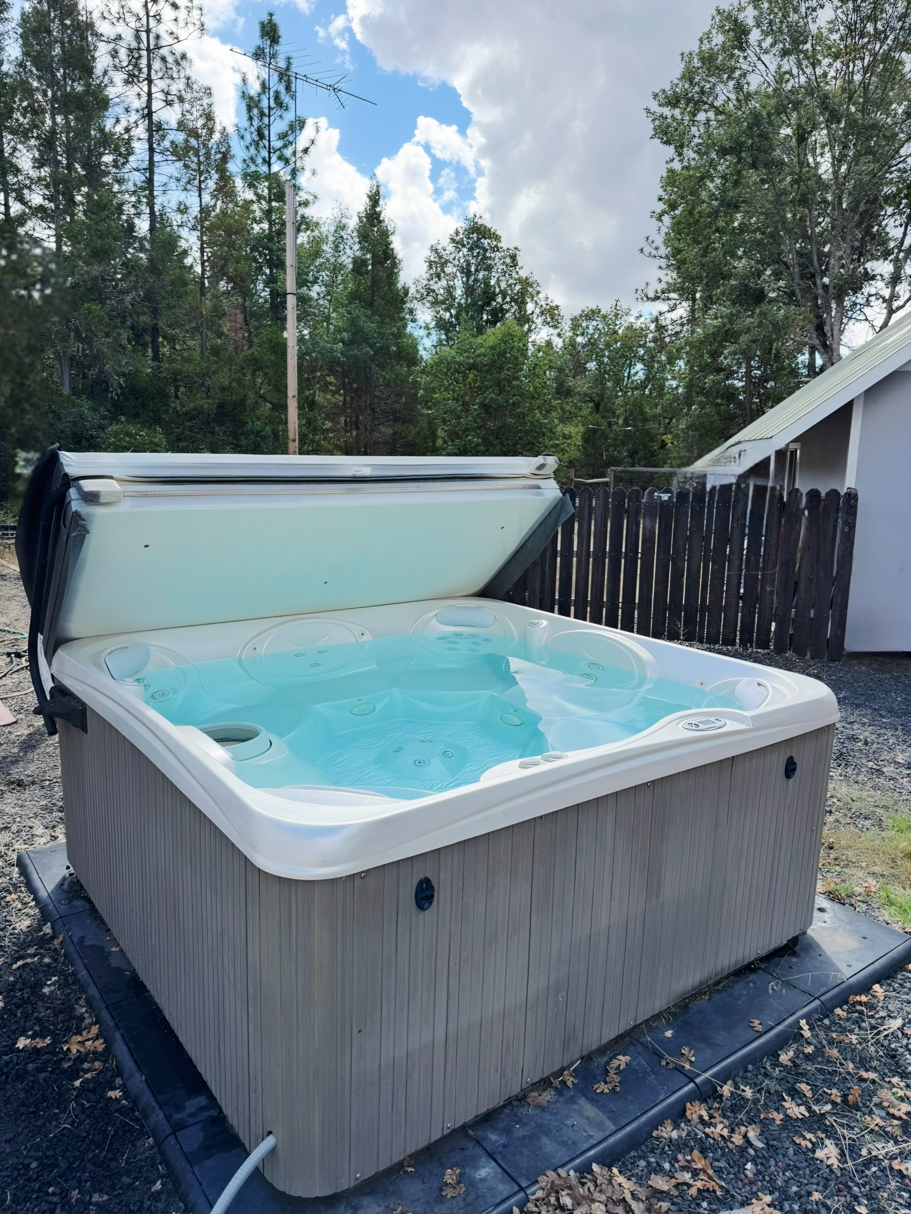 Outdoor hot tub with open cover showing crystal-clear, clean water surrounded by trees