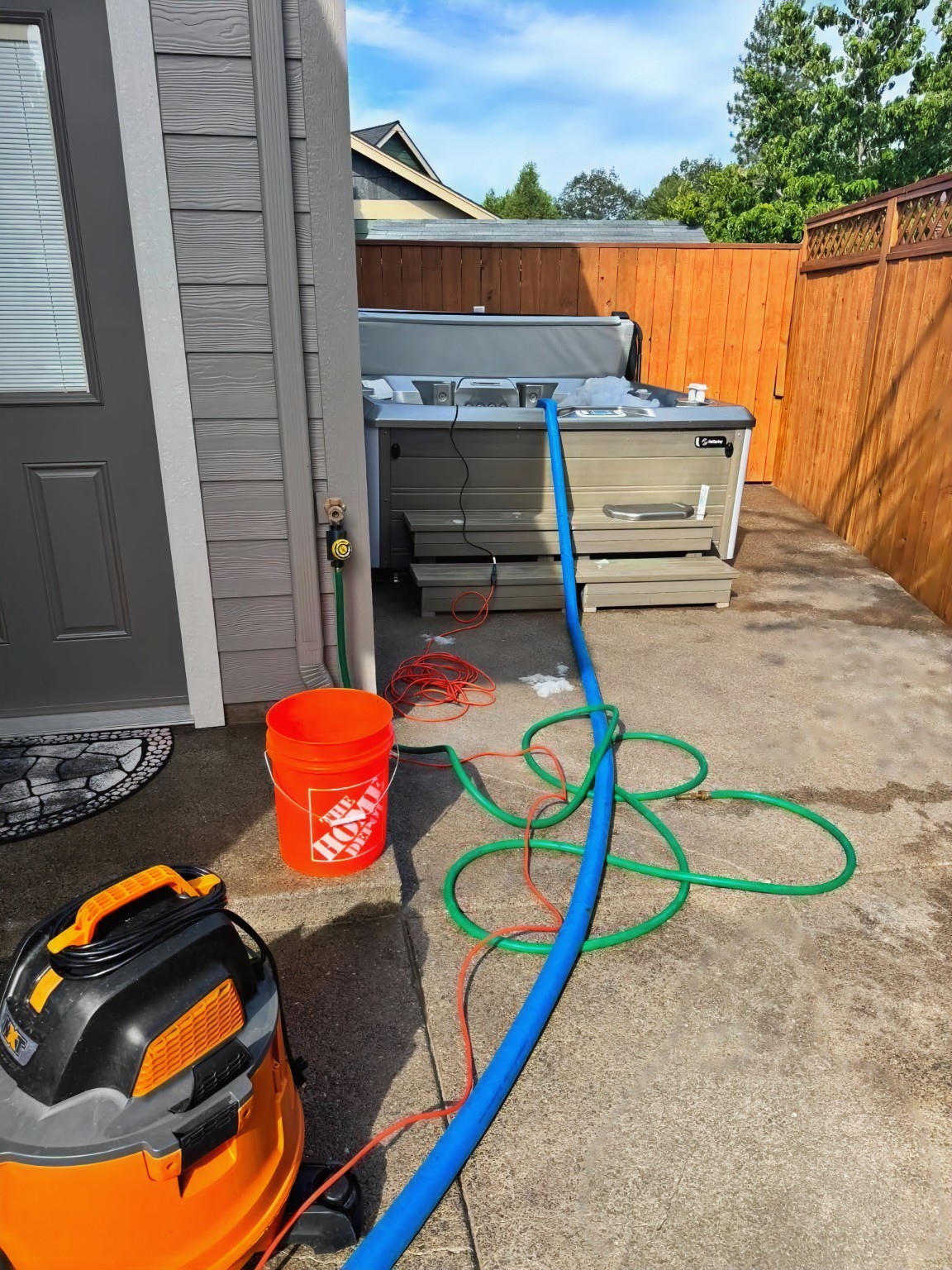 Outdoor hot tub on patio during drain and scrub service with drainage hose, bucket, and service equipment