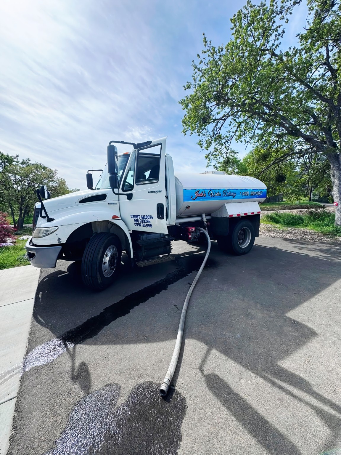 White commercial bulk water delivery tanker truck with delivery hose on driveway