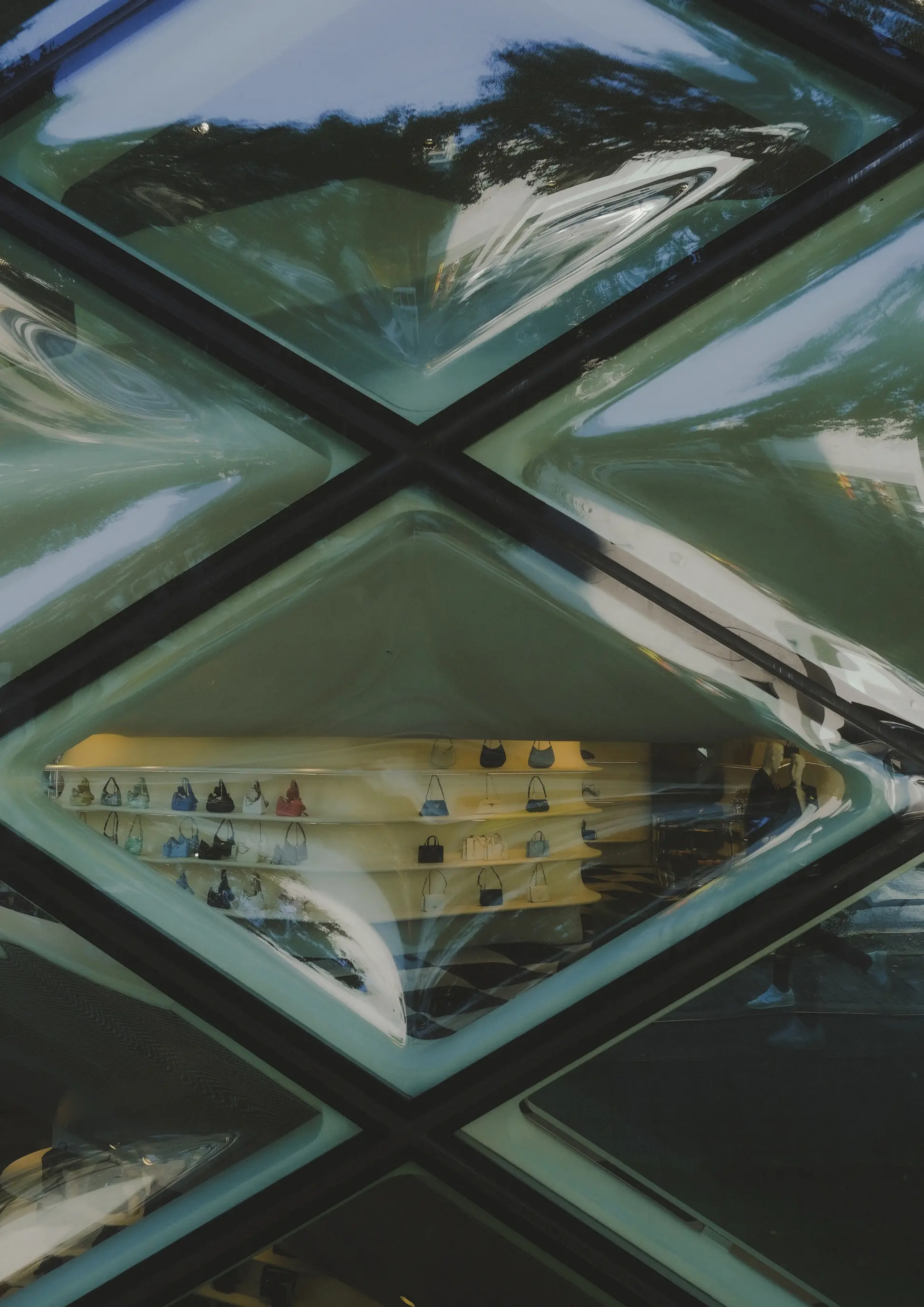 Diamond geometric faceted glass facade reflecting luxury handbag boutique interior and trees