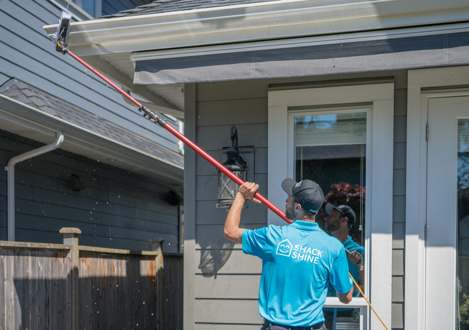Uniformed Shack Shine technician using a pole extension brush to wash the exterior face of home gutters and fascia