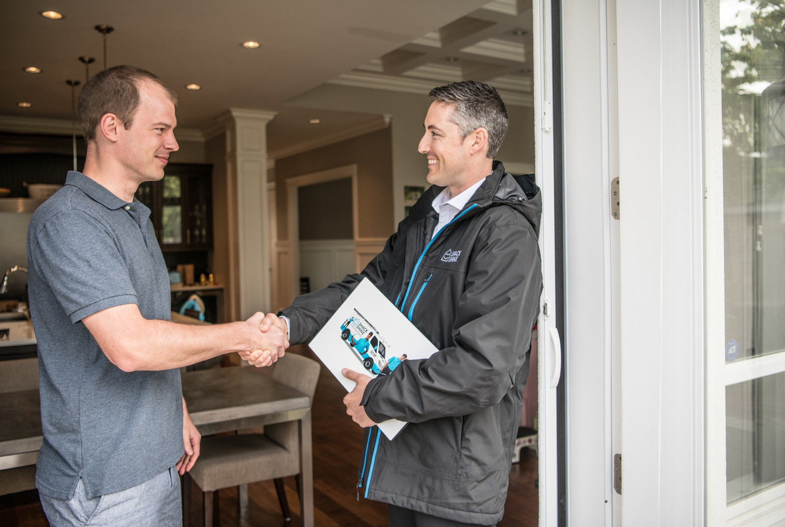 A friendly Shack Shine representative warmly greeting a customer with a handshake at their front door