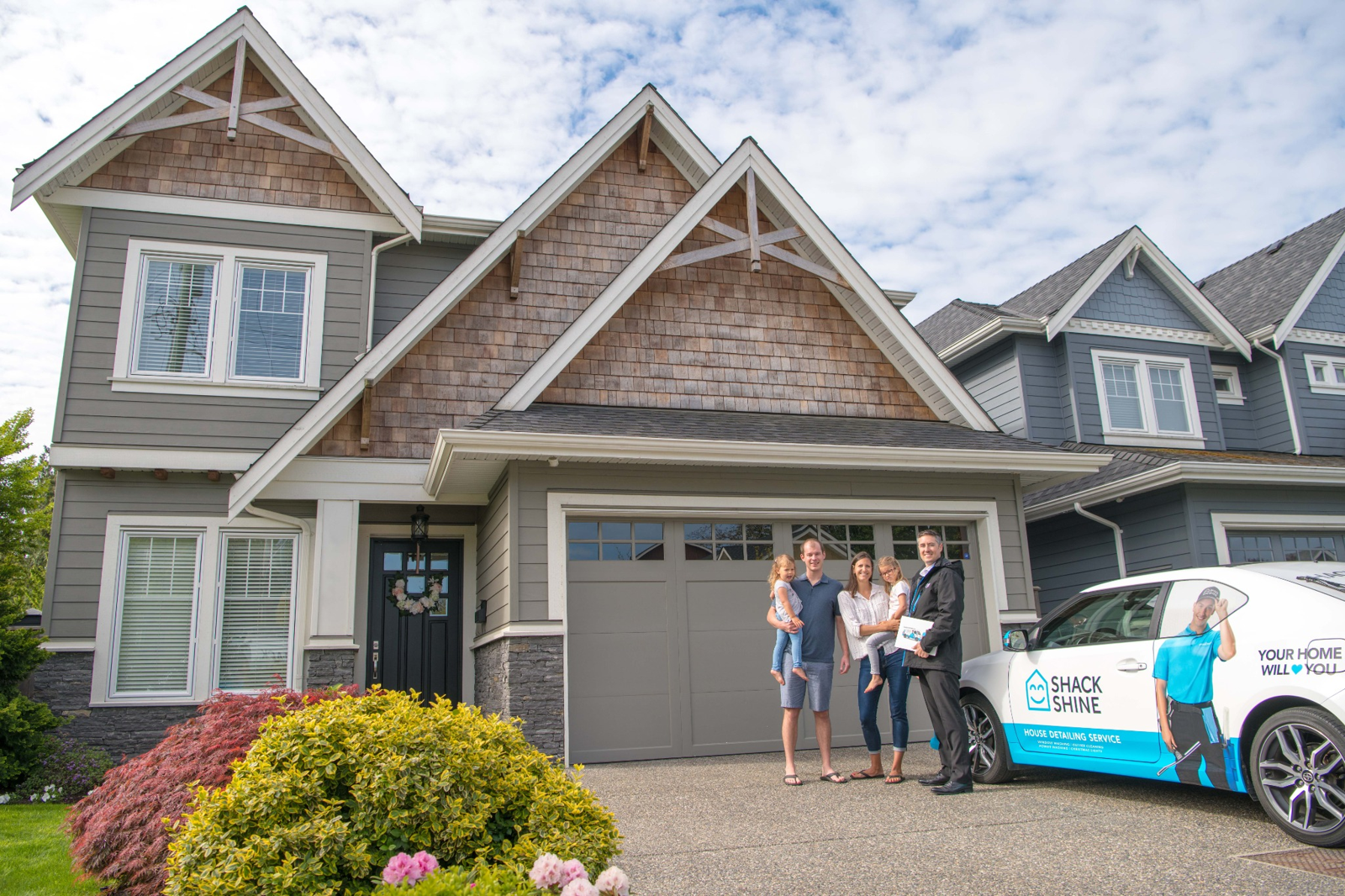 A smiling family and Shack Shine representative outside a beautiful home with the branded Shack Shine service car